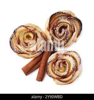 Roses de pomme fraîchement cuites et bâtonnets de cannelle isolés sur blanc, vue de dessus. Pâte feuilletée Banque D'Images