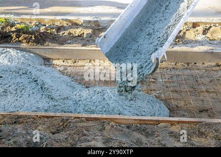 Un camion de malaxage de ciment verse du béton sur des barres d'acier renforcées pour la construction d'un nouveau trottoir Banque D'Images