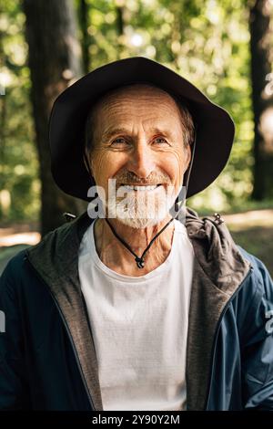 Gros plan d'un homme senior souriant portant un chapeau. Portrait d'un touriste mûr joyeux debout dans une forêt et regardant la caméra. Gros plan de Sen souriant Banque D'Images