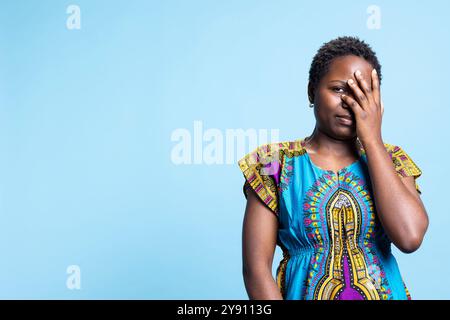 Femme anxieuse craintive cachant ses yeux de l'objectif par souci et peur due à quelque chose. African American Girl semble être un modèle terrifié effrayé et réticent en studio. Banque D'Images