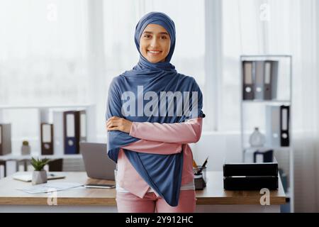 Femme d'affaires musulmane confiante debout avec les bras pliés près du lieu de travail au bureau Banque D'Images