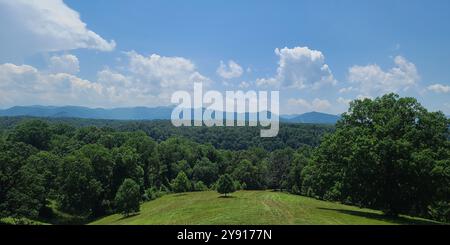Une vue panoramique d'un paysage verdoyant luxuriant avec des collines ondulantes et des montagnes lointaines sous un ciel bleu clair avec des nuages éparpillés. Banque D'Images