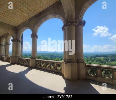 Une vue panoramique depuis un balcon en pierre avec des colonnes voûtées donnant sur un paysage verdoyant luxuriant sous un ciel bleu clair. Banque D'Images