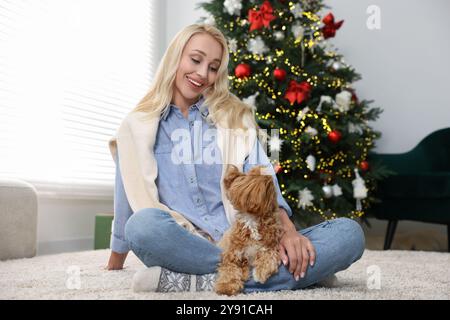 Femme avec chien mignon Maltipoo sur tapis dans la chambre décorée pour Noël Banque D'Images