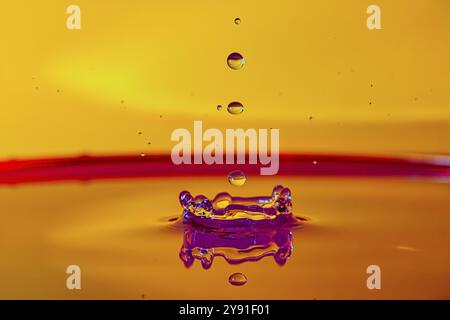 Des gouttes d'eau en ligne verticale créent une couronne sur une surface orange, photographie à grande vitesse, photographie de gouttes, Grenzach- Wyhlen, Baden-Wuer Banque D'Images