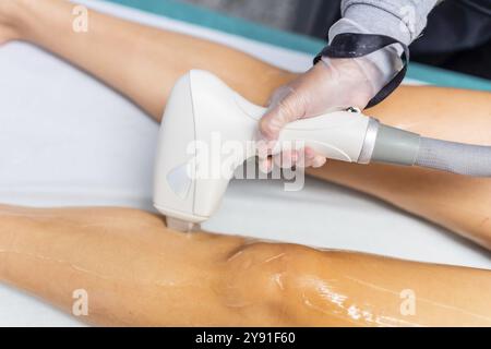 Photo rapprochée des jambes d'une patiente sur brancard pendant le traitement de beauté moderne à l'aide d'une machine laser d'épilation Banque D'Images