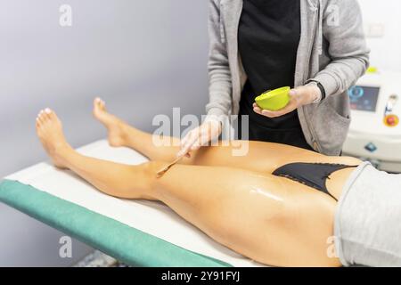Esthéticienne appliquant la crème aux jambes d'une femme pendant la procédure de laser pour enlever les cheveux Banque D'Images