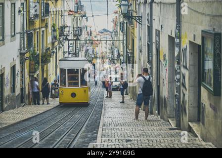 Un tramway jaune descend une ruelle escarpée et étroite pleine de charme dans un cadre urbain, les gens prenant des photos, Lisbonne, Portugal, Europe Banque D'Images