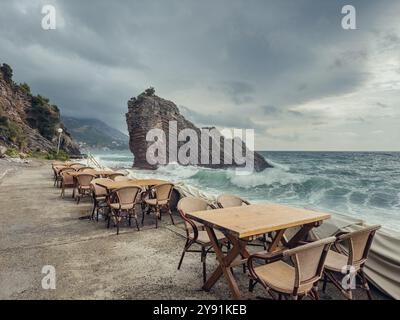 Café de plage vide à la journée nuageuse avec un grand rocher dans la mer, Rafailovici, Monténégro Banque D'Images