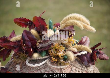 Un gros plan détaillé d'un bouquet d'automne rustique avec des feuilles rouges et brunes entrelacées avec un tissu en toile de jute, évoquant la chaleur et la beauté naturelle Banque D'Images