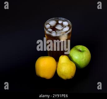 Jus de pomme et de poire de fruits de différentes variétés dans un grand verre avec de la glace sur fond noir, à côté de fruits mûrs. Gros plan. Banque D'Images
