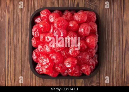 fruits confits, cerises séchées avec du sucre dans un bol carré sur une table rustique, vue de dessus. Banque D'Images