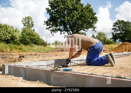 Gros plan d'un ouvrier maçonneur faisant du mortier de ciment sur un bloc de mur, fond flou. Concept de chantier de construction Banque D'Images