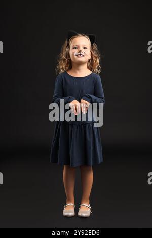 Fille drôle habillée comme chat pour la célébration d'Halloween sur fond noir Banque D'Images