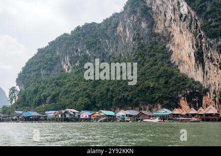 Phang Nga, Thaïlande - 26 octobre 2016 : maisons sur pilotis nichées à la base d'une falaise. Banque D'Images