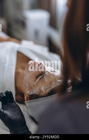 Le cosmétologue nettoie le visage de la jeune femme à l'aide de produits de soins de la peau professionnels. Photo de haute qualité Banque D'Images