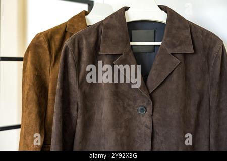 Deux vestes en daim en cuir marron de différentes nuances suspendues sur un cintre sur un fond blanc Banque D'Images