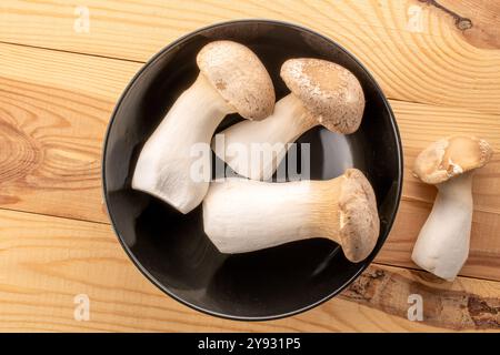 Champignon d'huître King parfumé frais dans une assiette en céramique sur une table en bois, macro, vue de dessus. Banque D'Images