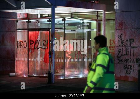 Guildford, Angleterre, Royaume-Uni. 8 octobre 2024. Un agent de sécurité regarde la peinture et les graffitis sur les portes d'entrée. Palestine action cible les succursales d'assurance Allianz dans tout le Royaume-Uni, brisant leurs fenêtres, pulvérisant l'extérieur de leurs succursales avec de la peinture et des graffitis sur les bâtiments. L'action palestinienne vise Allianz parce qu'ils assurent et investissent dans la société israélienne d'armement Elbit Systems, ils exigent que la société abandonne Elbit Systems. Crédit : ZUMA Press, Inc/Alamy Live News Banque D'Images