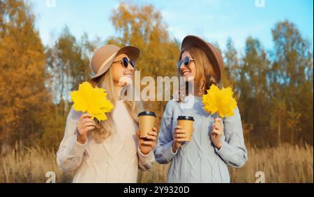 Portrait de jeunes amis heureux deux femmes avec des feuilles jaunes d'automne, élégantes copines souriantes ensemble à l'extérieur, dans un parc ensoleillé, saison d'automne Banque D'Images