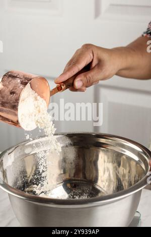 Concept de cuisson à la main femelle versant la farine dans le bol à mélanger en acier inoxydable Banque D'Images