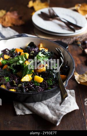 Ambiance automnale rustique avec nouilles de riz noires, citrouille et plat de chou frisé sur une table en bois, mettant en valeur la richesse de la saison avec des tons terreux. Banque D'Images