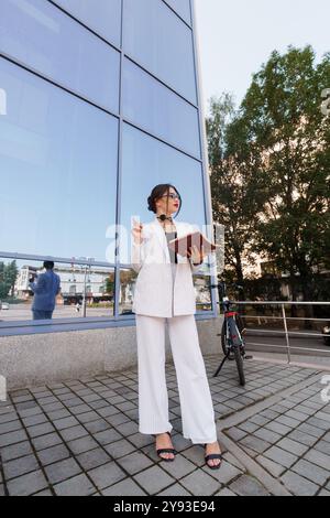 Femme d'affaires confiante posant élégamment dans le costume Pinstripe par Modern Glass Building. Banque D'Images