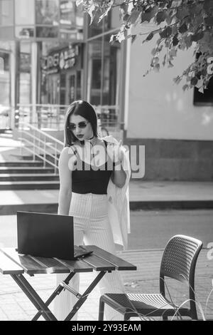 Femme d'affaires élégante dans les lunettes de soleil à l'espace de travail extérieur avec ordinateur portable. Banque D'Images