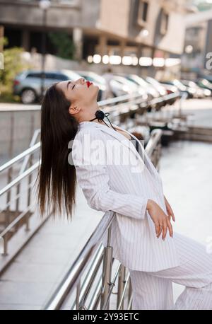 Femme élégante en costume rayé posant en toute confiance à l'extérieur. Banque D'Images