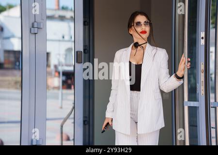 Femme d'affaires élégante dans un costume rayé élégant sortant de l'immeuble de bureaux moderne. Banque D'Images