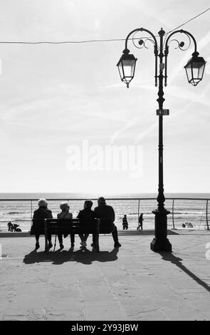 Black and white photo. Three senior ladies and a gentleman resting on a bench on the promenade of the holiday resort, Alassio, Savona, Liguria, Italy Stock Photo