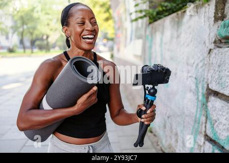 Vlogger sportive tenant son appareil photo et son tapis d'exercice dans la ville Banque D'Images