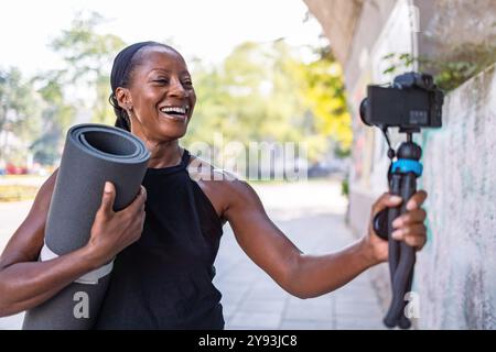 Vlogger sportive tenant son appareil photo et son tapis d'exercice dans la ville Banque D'Images