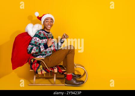 Portrait pleine longueur de gentil jeune homme présent sack ride traîneau vide Spacenew année xmas isolé sur fond de couleur jaune Banque D'Images