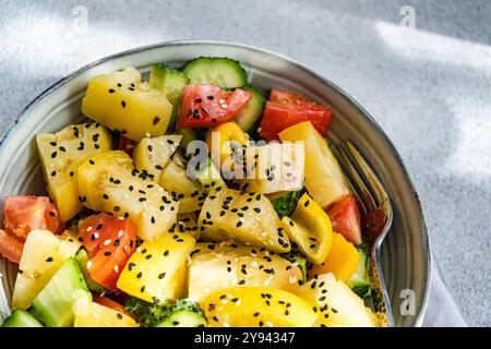 Vue de dessus d'une salade de légumes colorée avec tomates rouges et jaunes, concombres, poivrons et saupoudrée de graines de sésame, servie dans un bol. Banque D'Images
