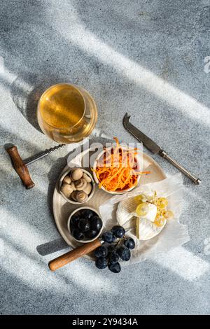 Vue de dessus d'un plateau de brie fumé accompagné d'olives fermentées, de champignons marinés, de carottes râpées et d'un verre de vin blanc sec, présen Banque D'Images