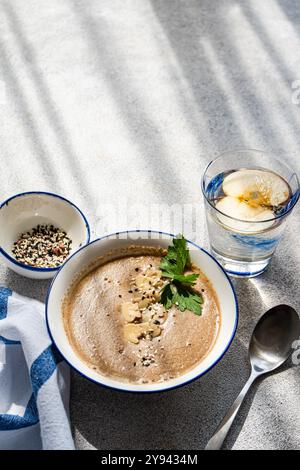 Vue de dessus d'un dîner sain avec soupe à la crème de champignons garnie de graines et d'herbes, à côté d'un verre d'eau infusée de pomme biologique Banque D'Images