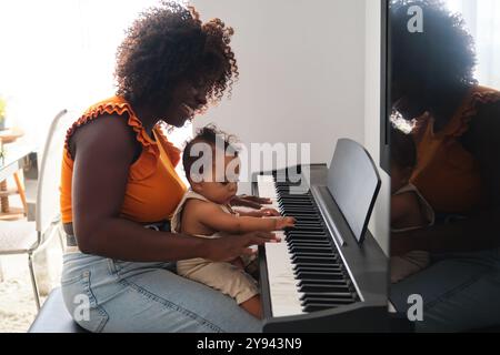 Une image réconfortante d'une mère africaine aidant sa petite fille à jouer du piano à partager un moment de joie et d'apprentissage dans une pièce très éclairée Banque D'Images