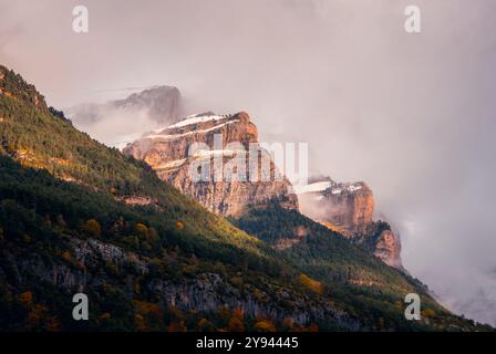 Une vue captivante sur les Pyrénées aragonaises en automne, affichant un feuillage vibrant contre de majestueux sommets enneigés partiellement enveloppés dans un m doux Banque D'Images