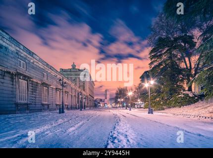 La neige recouvre les sentiers et l'architecture historique près du Palais Royal de Madrid, en Espagne, sous un ciel nocturne magnifiquement coloré Banque D'Images