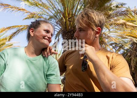 Un couple profite d’une journée ensoleillée dans un parc entouré de palmiers, souriant et partageant un moment d’amour ensemble à l’ombre Banque D'Images