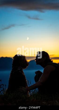 Femme avec chien profitant d'un coucher de soleil dans les Alpes suisses, près du lac Léman. Un moment serein capturé sous le ciel du soir. Banque D'Images