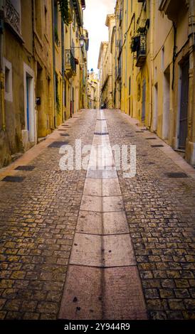 Charmante rue pavée bordée de vieux bâtiments colorés sous un ciel nuageux dans le sud de la France, reflétant l'architecture européenne classique Banque D'Images