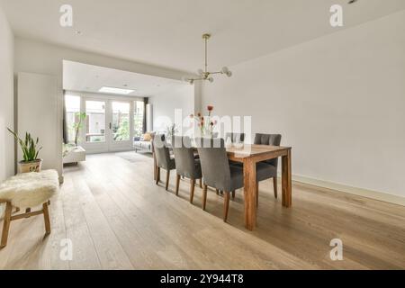 Cette salle à manger moderne, spacieuse et lumineuse, dispose d''une table en bois, de chaises rembourrées grises et d''un éclairage naturel. Banque D'Images