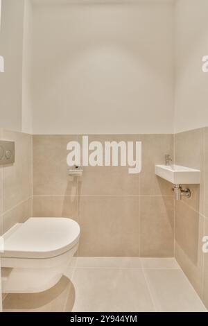 Salle de bains contemporaine avec toilettes murales et lavabo d'angle avec murs carrelés et sol aux tons neutres. Banque D'Images