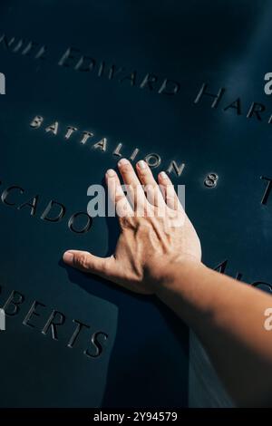 Gros plan d'une main touchant un nom sur une plaque commémorative à New York, en l'honneur des héros du 11 septembre. La lumière du soleil jette une lueur chaude sur le nam gravé Banque D'Images