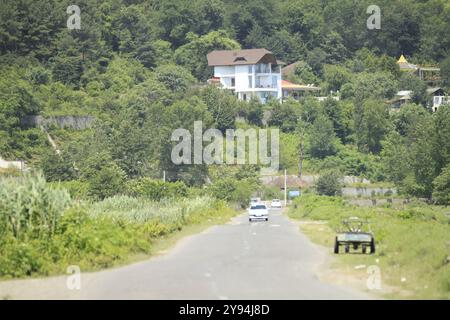 Route sinueuse à travers un paysage verdoyant menant à une maison à flanc de colline. Route de campagne, route panoramique. Banque D'Images