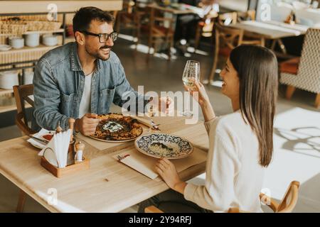 Deux personnes savourent leurs boissons à une table en bois, immergées dans une ambiance de restaurant détendue, tout en étant profondément dans la conversation et les rires. Banque D'Images