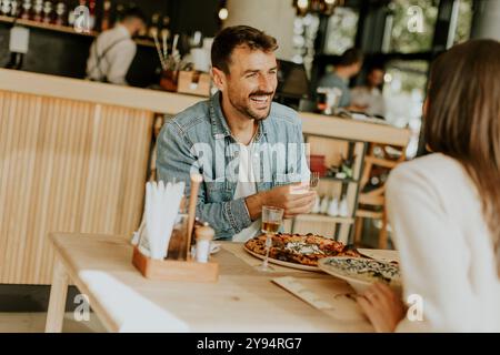 Un couple s'engage dans une conversation animée tout en savourant une délicieuse cuisine dans un restaurant lumineux, partageant des rires et des moments de connexion sur un lei Banque D'Images