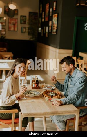 Un couple s'engage dans une conversation animée tout en savourant une délicieuse cuisine dans un restaurant lumineux, partageant des rires et des moments de connexion sur un lei Banque D'Images